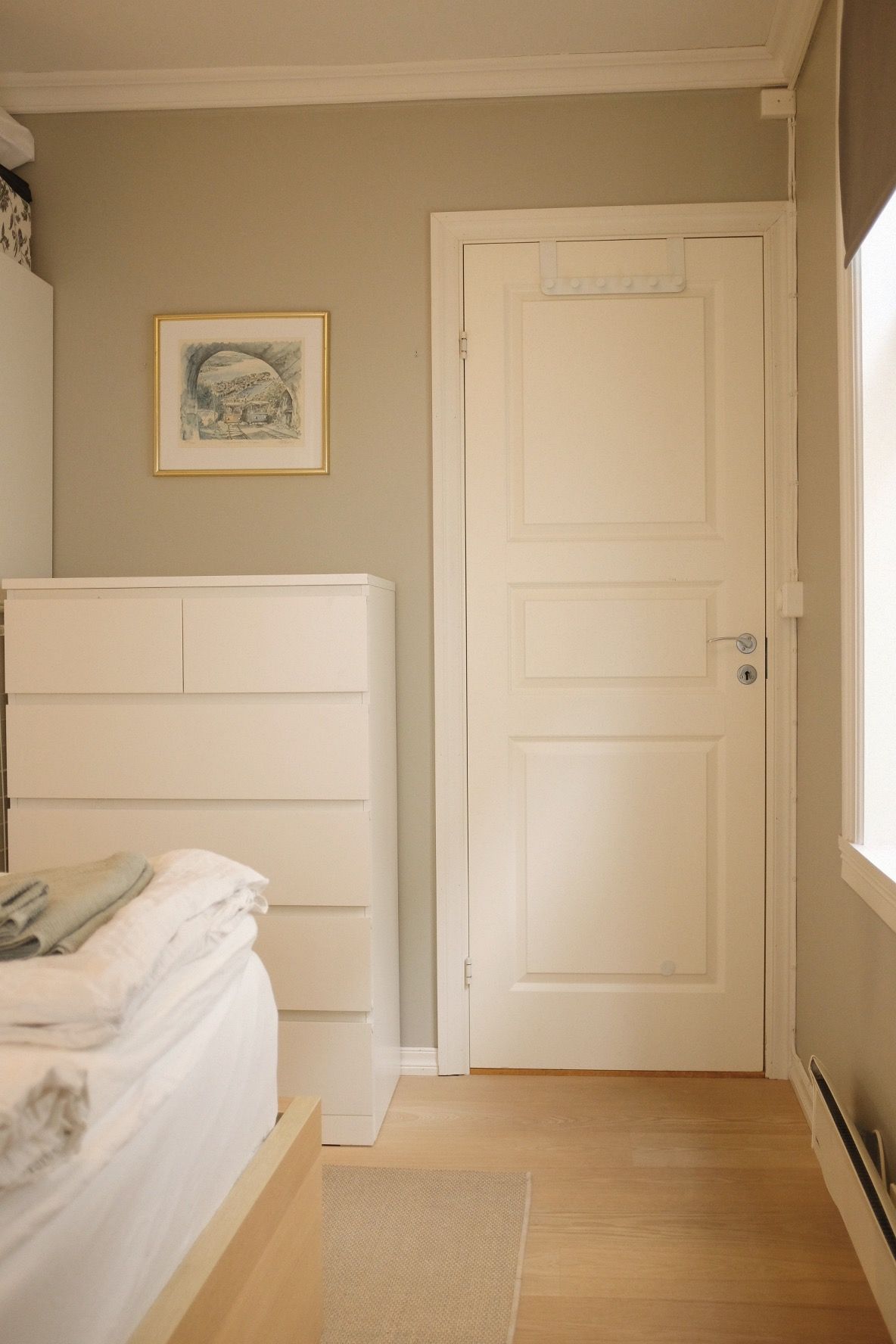 Een slaapkamer met een bed, een deur en een lijst met een afbeelding aan de muur.