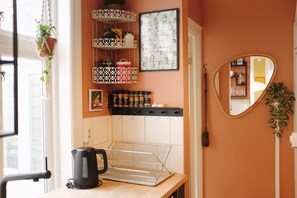 Une cuisine équipée d’une bouilloire, d’étagères remplies d’épices, d’un tableau encadré et d’un miroir.