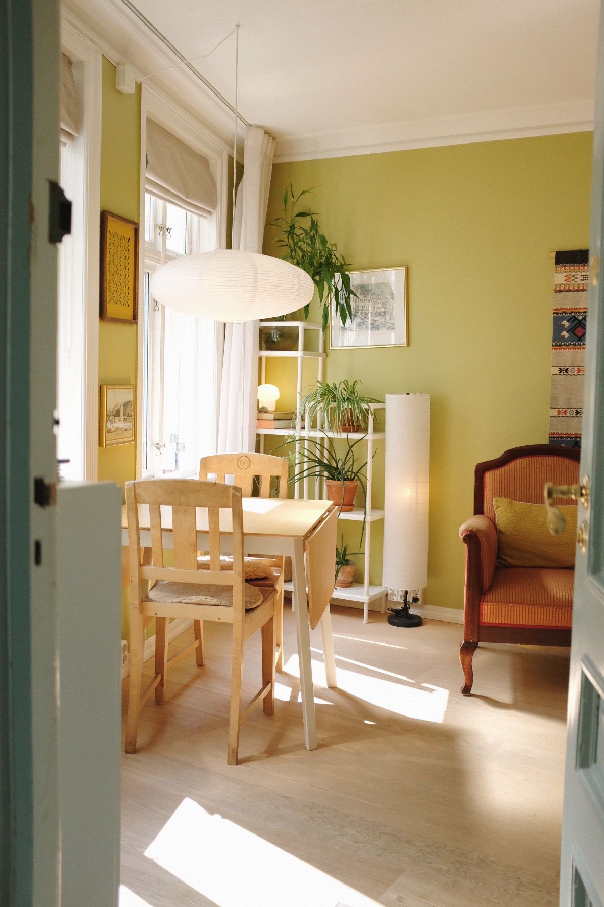 Een eetgedeelte met een houten tafel en stoelen, een hanglamp, een potplant en een stoel met kussen.