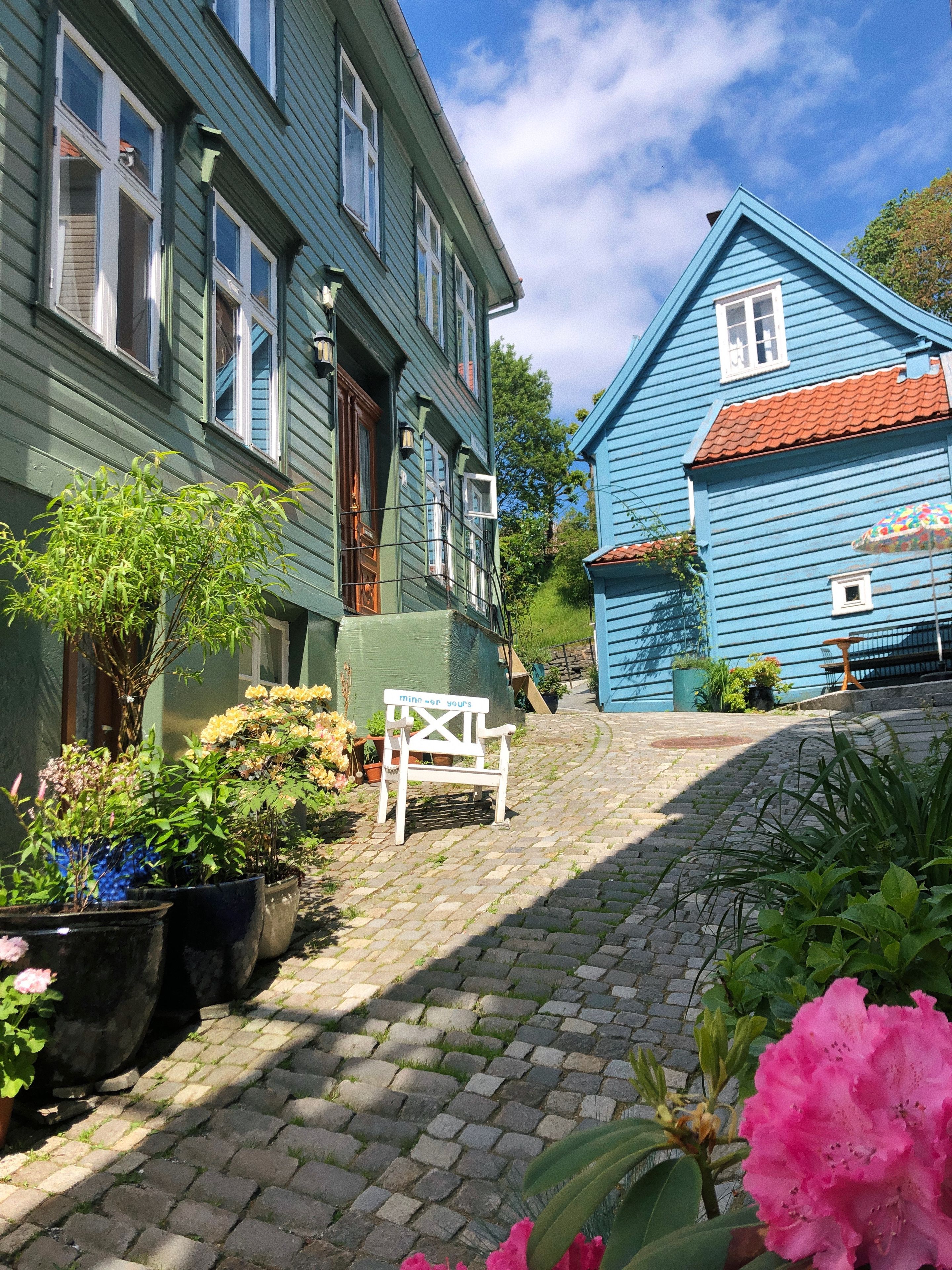 A courtyard with a cobblestone path, a bench, potted plants, and two buildings with distinct architectural styles.