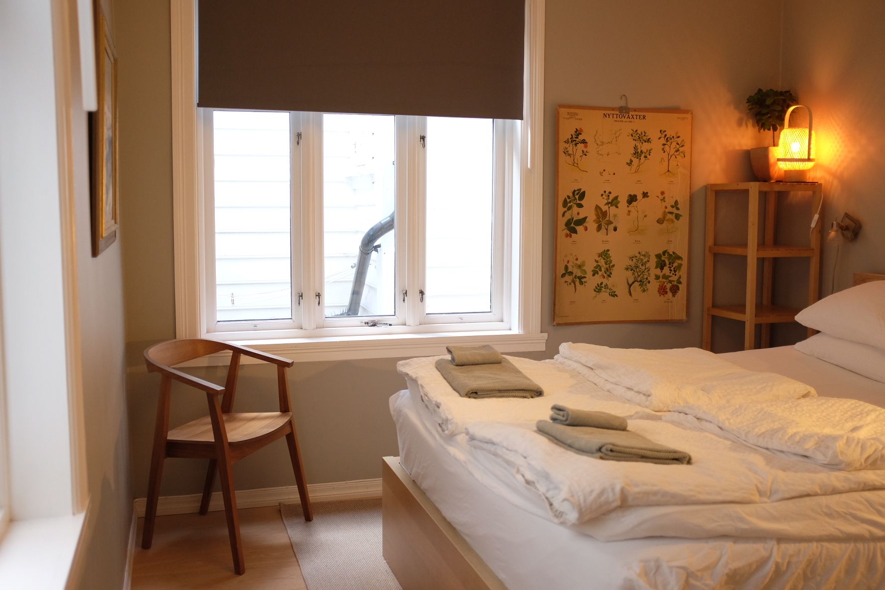 A bedroom with a bed, a chair, a window, a wall-mounted plant, and a wall-mounted lamp.