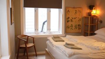 A bedroom with a bed, a chair, a window, a wall-mounted plant, and a wall-mounted lamp.