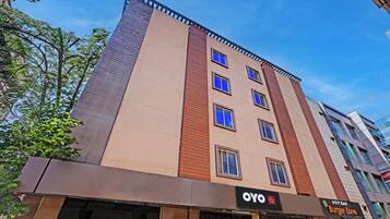 Un immeuble à plusieurs étages doté d’une façade sobre, de plusieurs fenêtres et d’une devanture avec une enseigne indiquant « OYO » et « Burger Zone ».