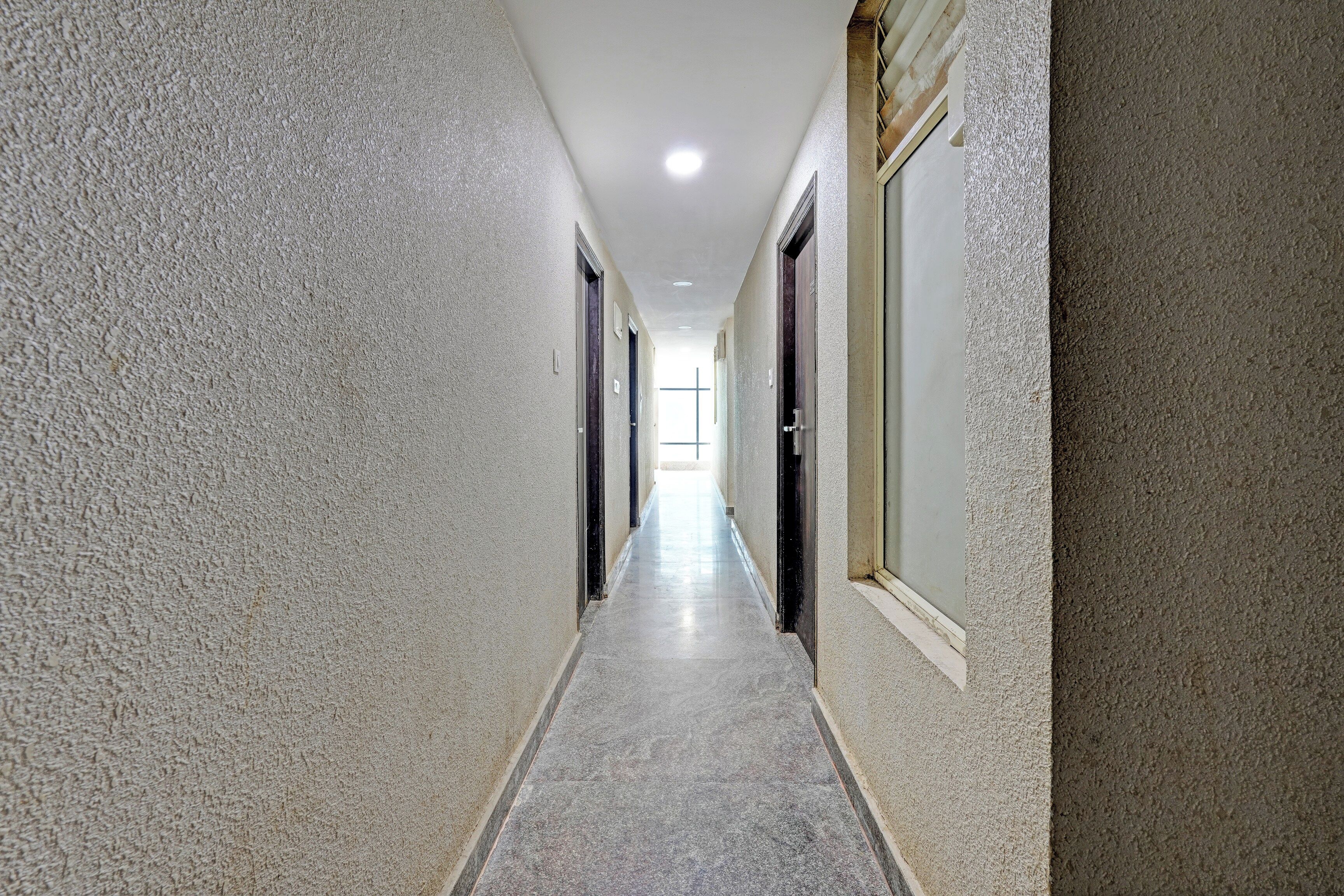 A long, narrow hallway with textured walls and a tiled floor, leading to a door at the end.