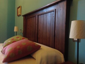Ein Schlafzimmer mit einem hölzernen Kopfteil, einem Bett mit rosa und gelben Kissen, einer Nachttischlampe und einem gerahmten Bild an der Wand.