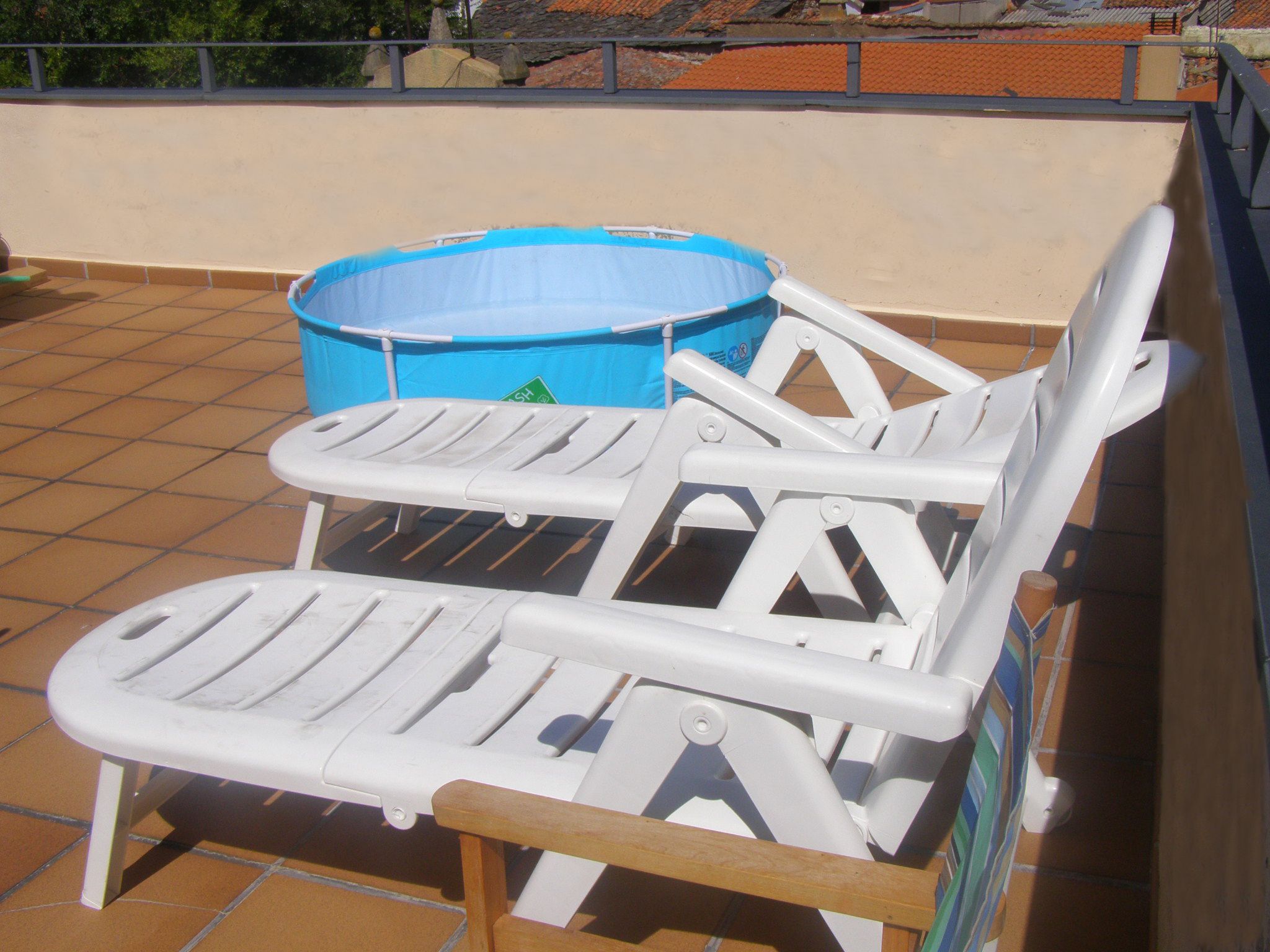 A rooftop terrace with a blue inflatable pool and two white lounge chairs.