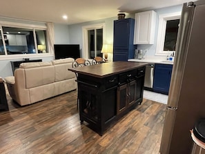 A modern kitchen with a central island, dark cabinetry, and a beige sofa in the living area. - Modern 5-Acre Barn Loft • Mt. Rainier & Crystal Mountain Basecamp • Pet Friendly (Enumclaw)