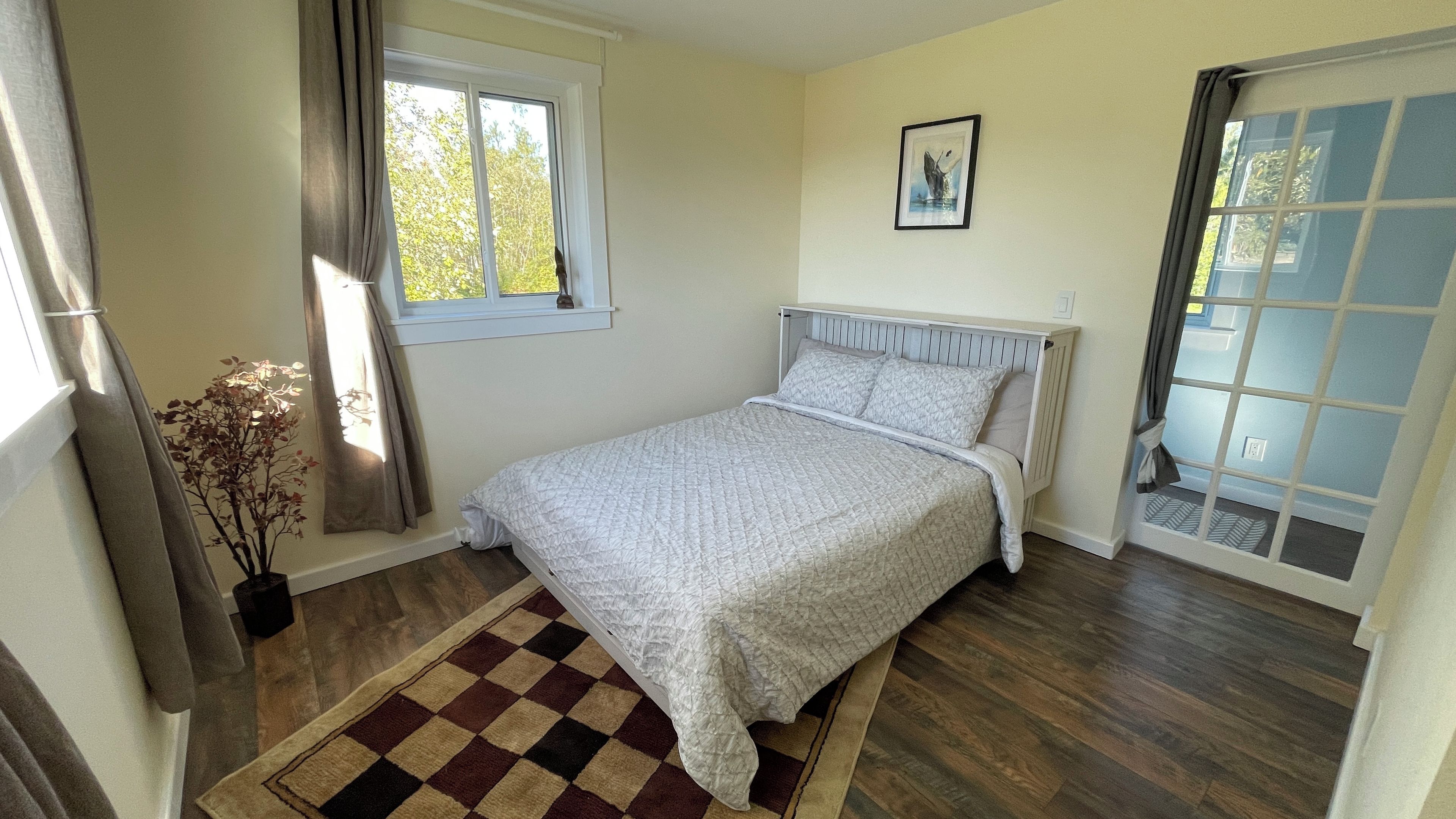 A bedroom with a bed, a window, a door, and a checkered rug.