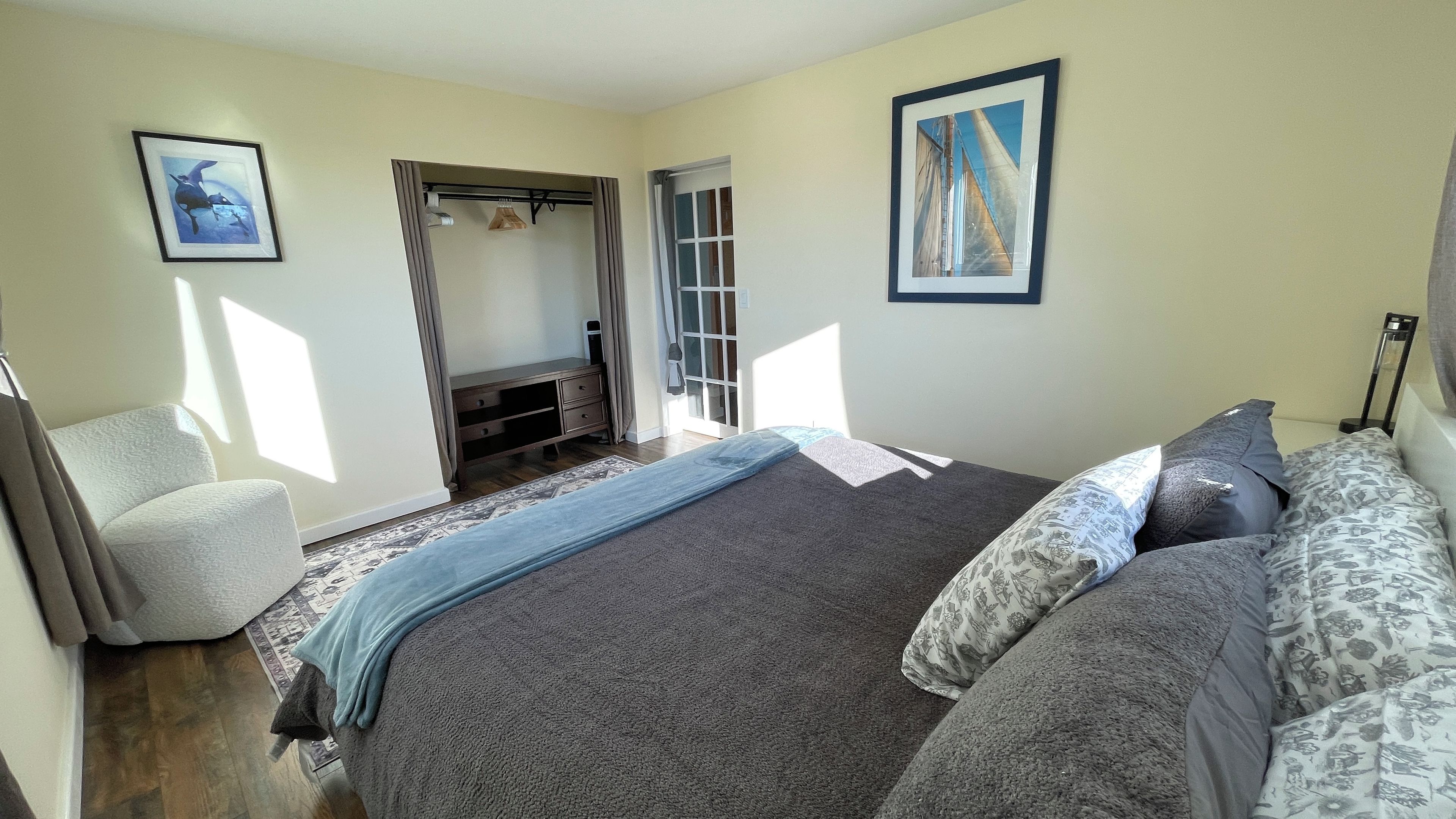 A bedroom with a bed, a chair, a wardrobe, and a door leading to another room.