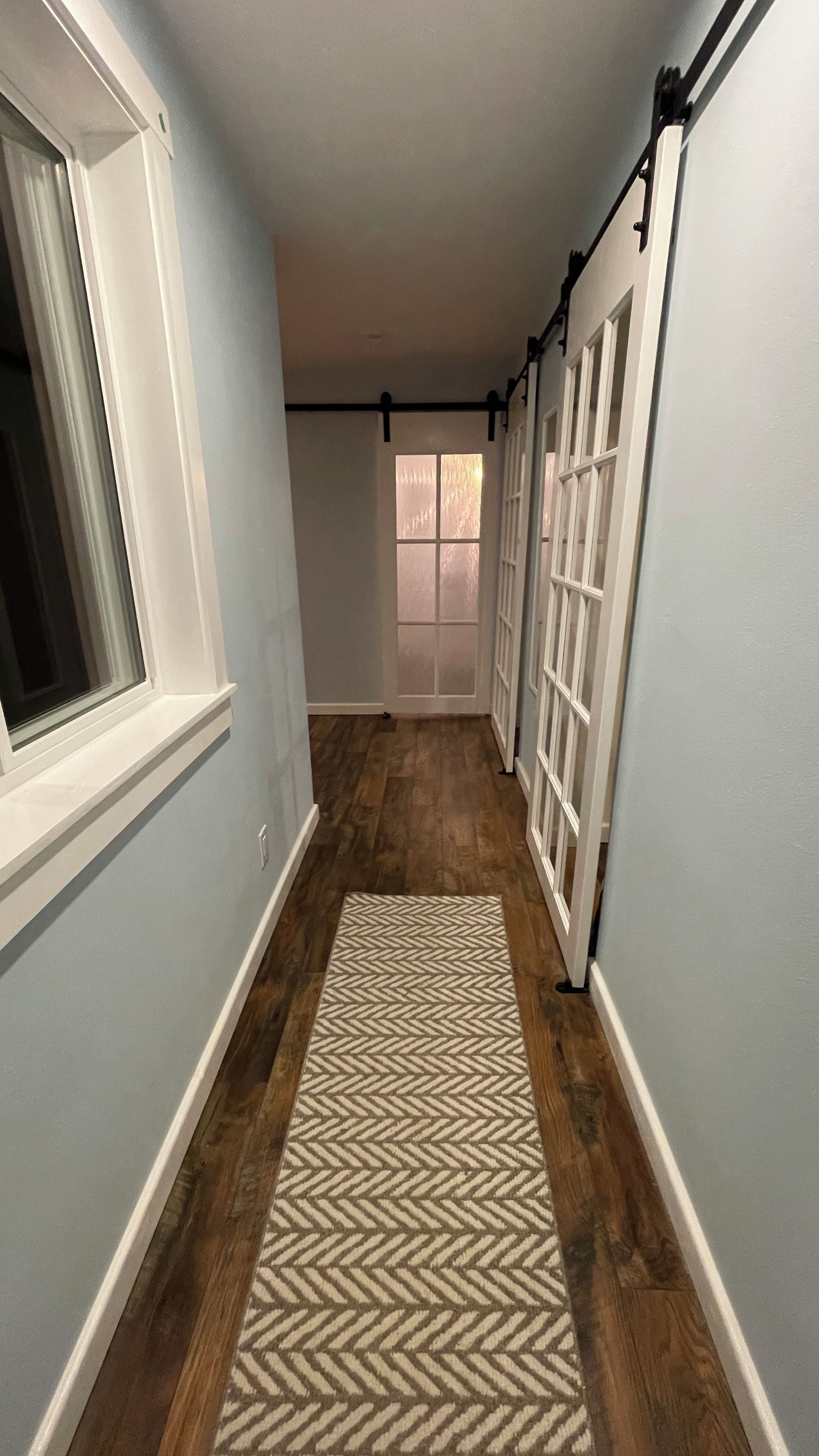 A hallway with a wooden floor, a patterned rug, and a door with frosted glass panels.