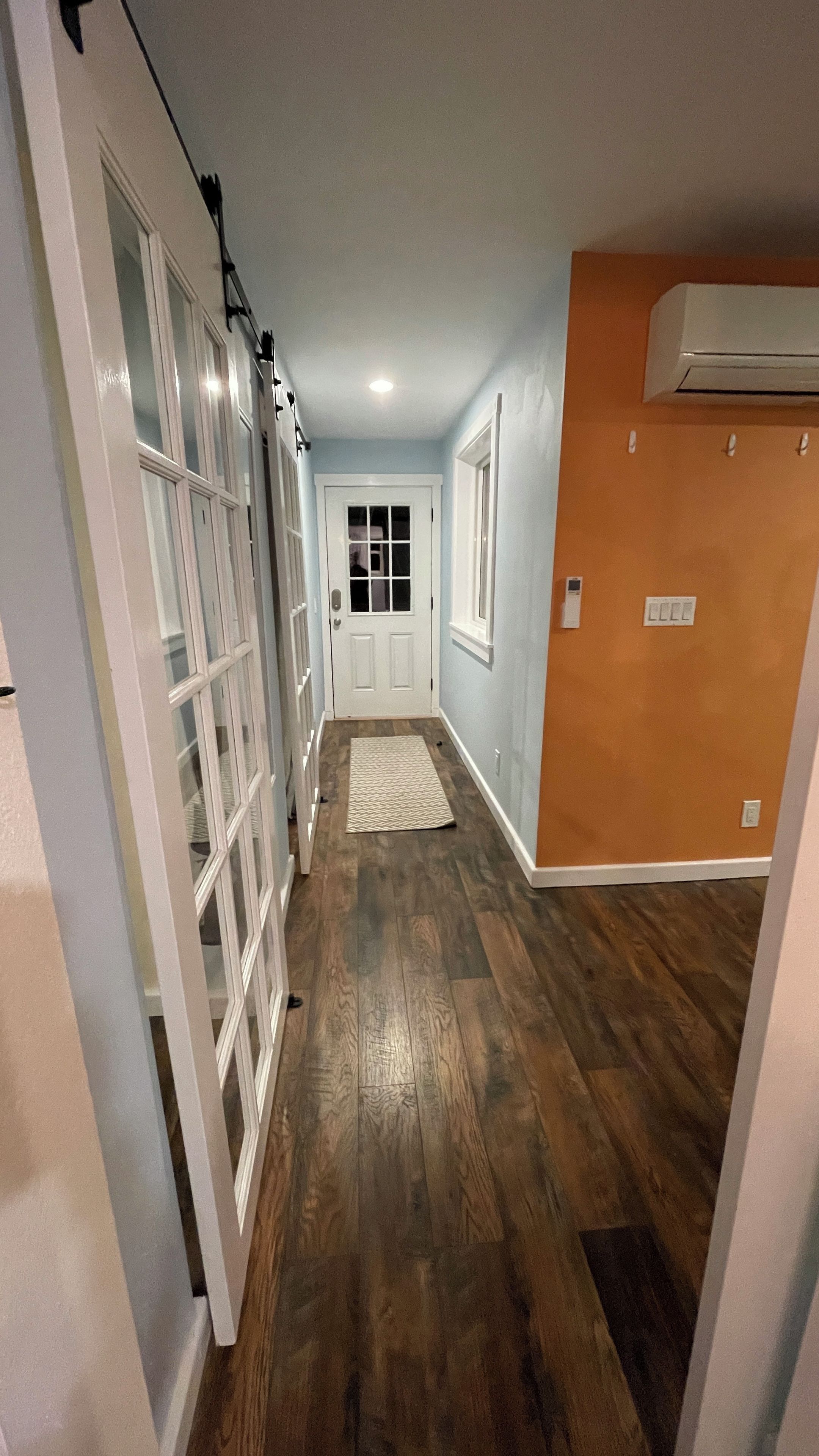 A hallway with wooden flooring, a door at the end, and an air conditioning unit on the wall.