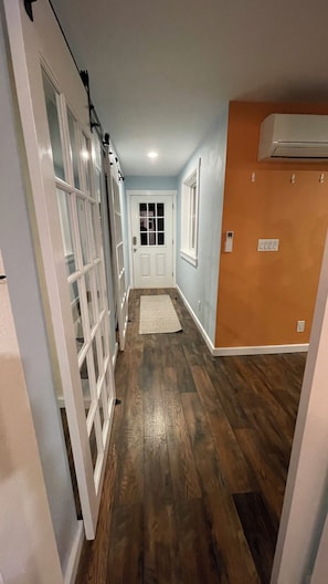 A hallway with wooden flooring, a door at the end, and an air conditioning unit on the wall. - Modern 5-Acre Barn Loft • Mt. Rainier & Crystal Mountain Basecamp • Pet Friendly (Enumclaw)