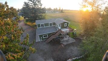 A two-story house with a front deck, a driveway, and a tractor in the yard.