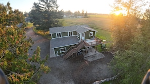 A two-story house with a front deck, a driveway, and a tractor in the yard. - Modern 5-Acre Barn Loft • Mt. Rainier & Crystal Mountain Basecamp • Pet Friendly (Enumclaw)