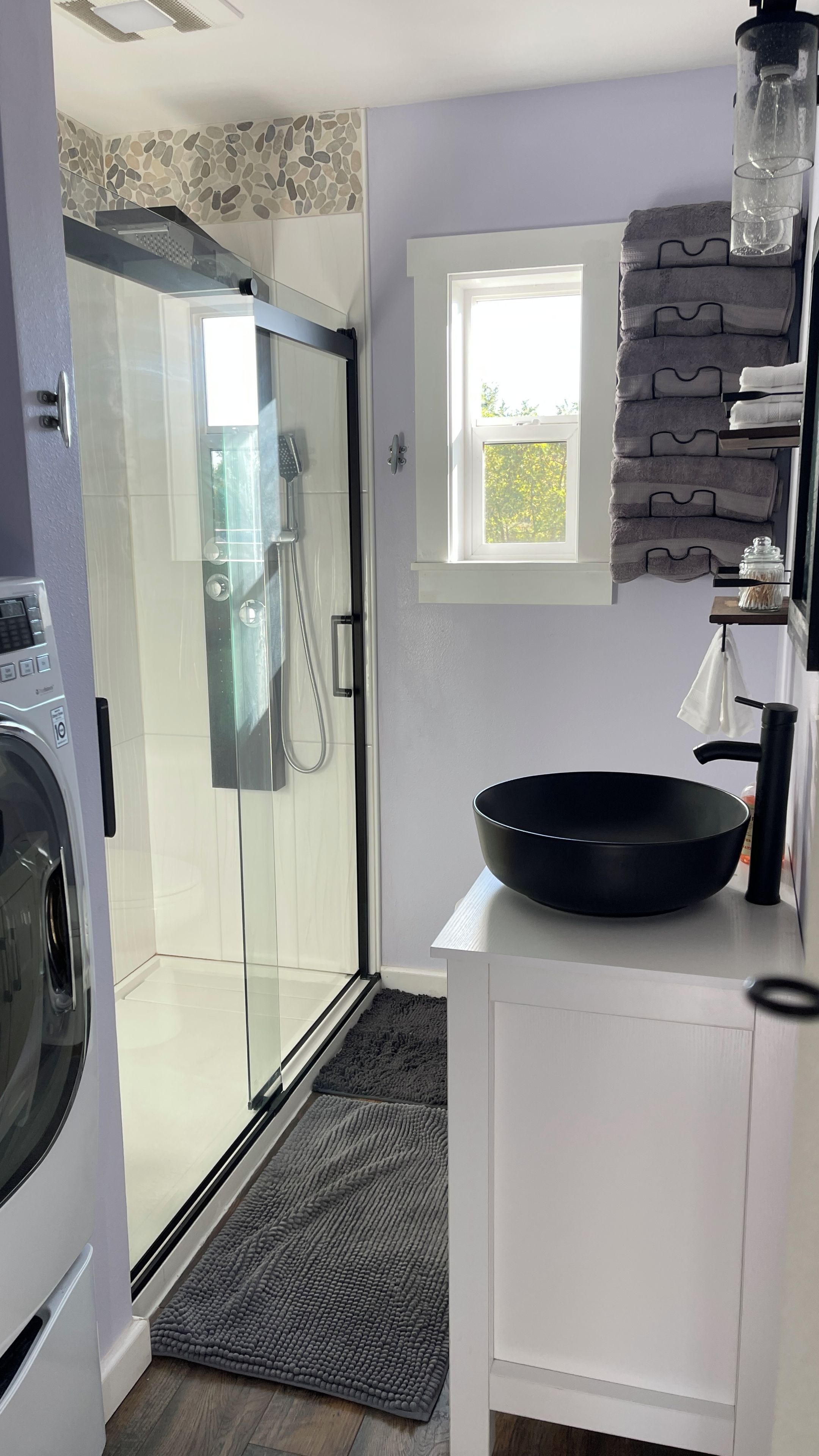 A modern kitchen with a glass shower door, a black bowl on the countertop, and a window with a view of greenery.
