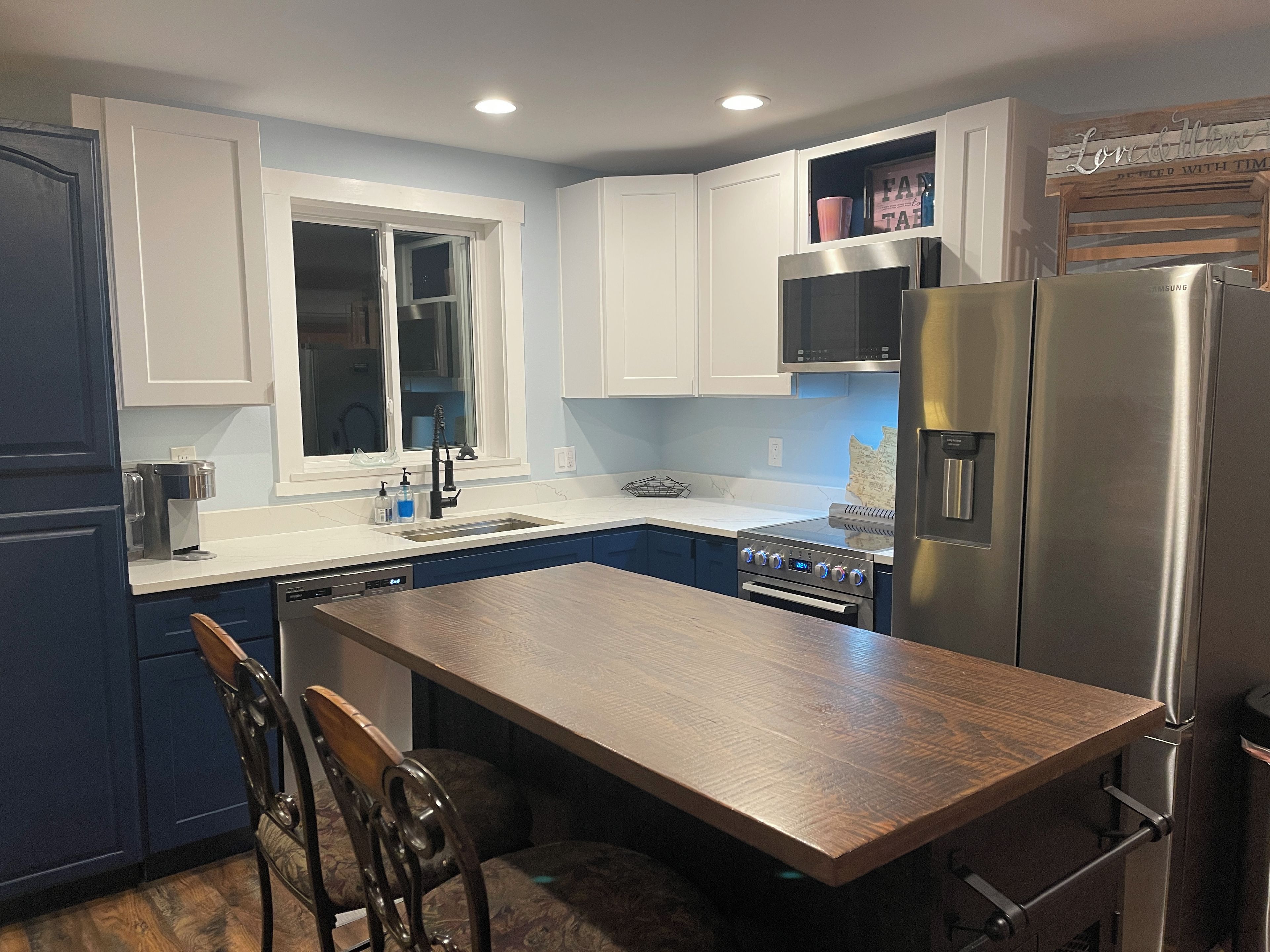A modern kitchen with white cabinets, a stainless steel refrigerator, and a wooden dining table.
