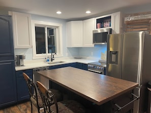 A modern kitchen with white cabinets, a stainless steel refrigerator, and a wooden dining table. - Modern 5-Acre Barn Loft • Mt. Rainier & Crystal Mountain Basecamp • Pet Friendly (Enumclaw)