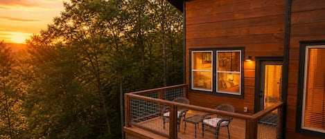 A wooden cabin with a balcony, two windows, and a chair.
