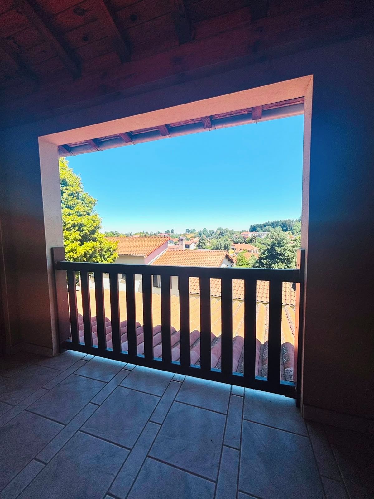 Un balcon donnant sur un quartier résidentiel, avec des balustrades en bois et un sol carrelé.