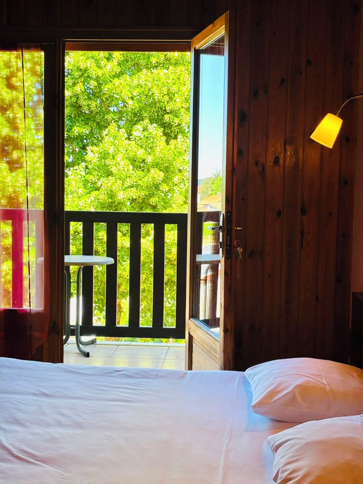 A bedroom with a bed, a wooden door leading to an outdoor balcony, and a small table.