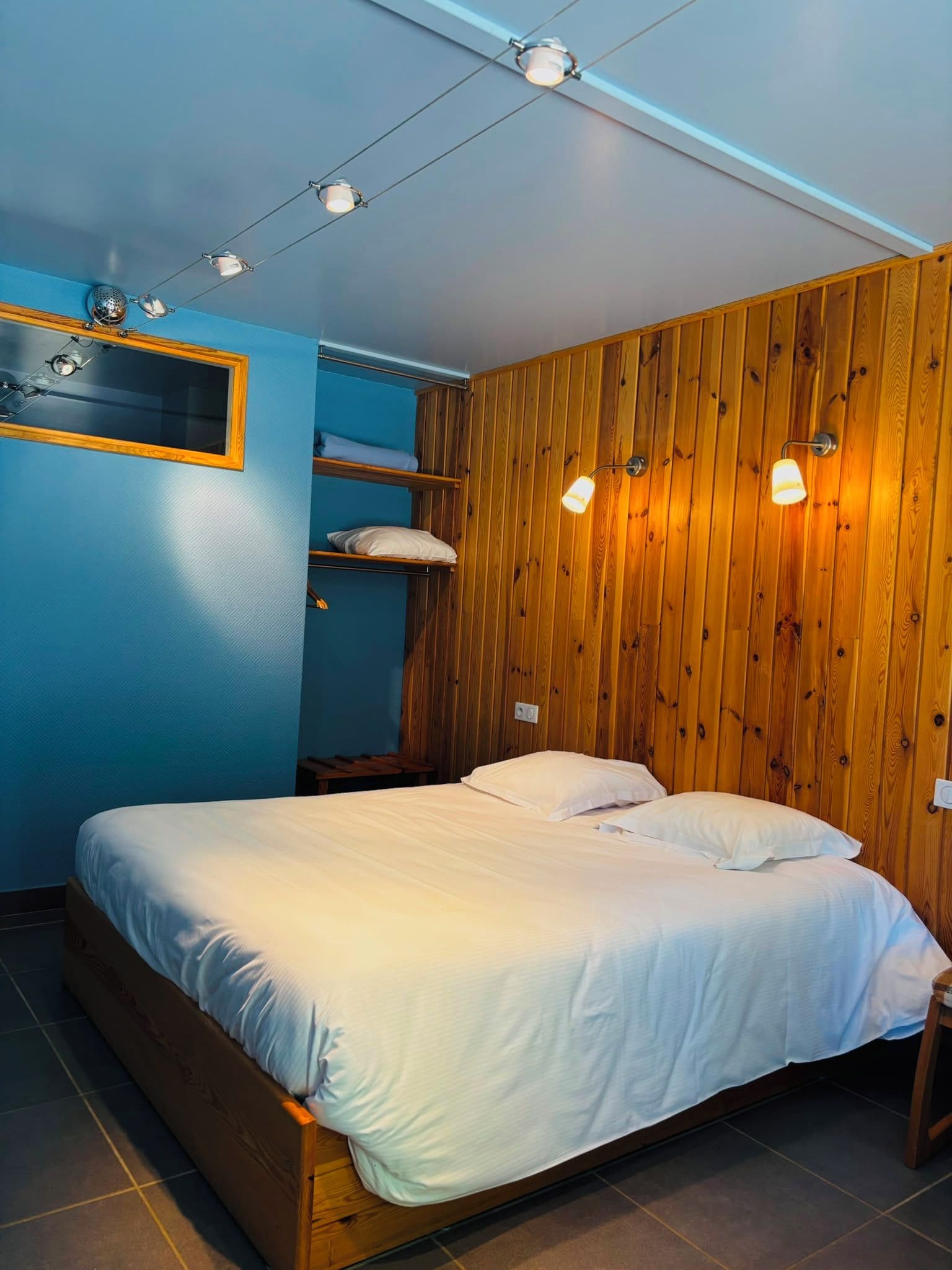 Uma cama de solteiro com roupa de cama branca em um quarto com paredes azuis e painéis de madeira.