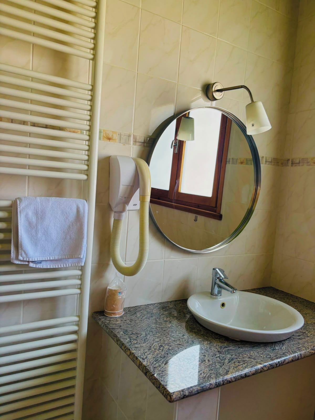 A bathroom with a white sink, a round mirror with a light, a towel rack, and a hairdryer.
