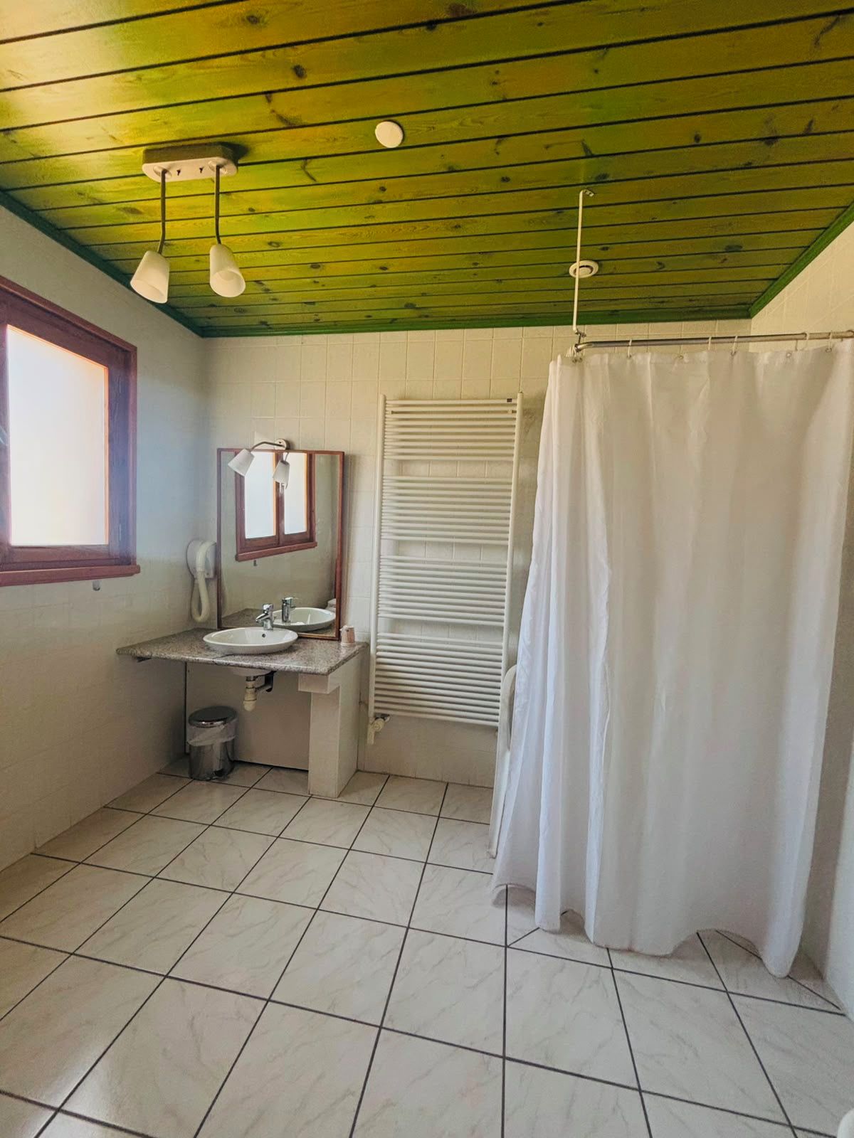 Une salle de bain avec un sol carrelé, un lavabo, un miroir, un porte-serviettes et un rideau de douche.