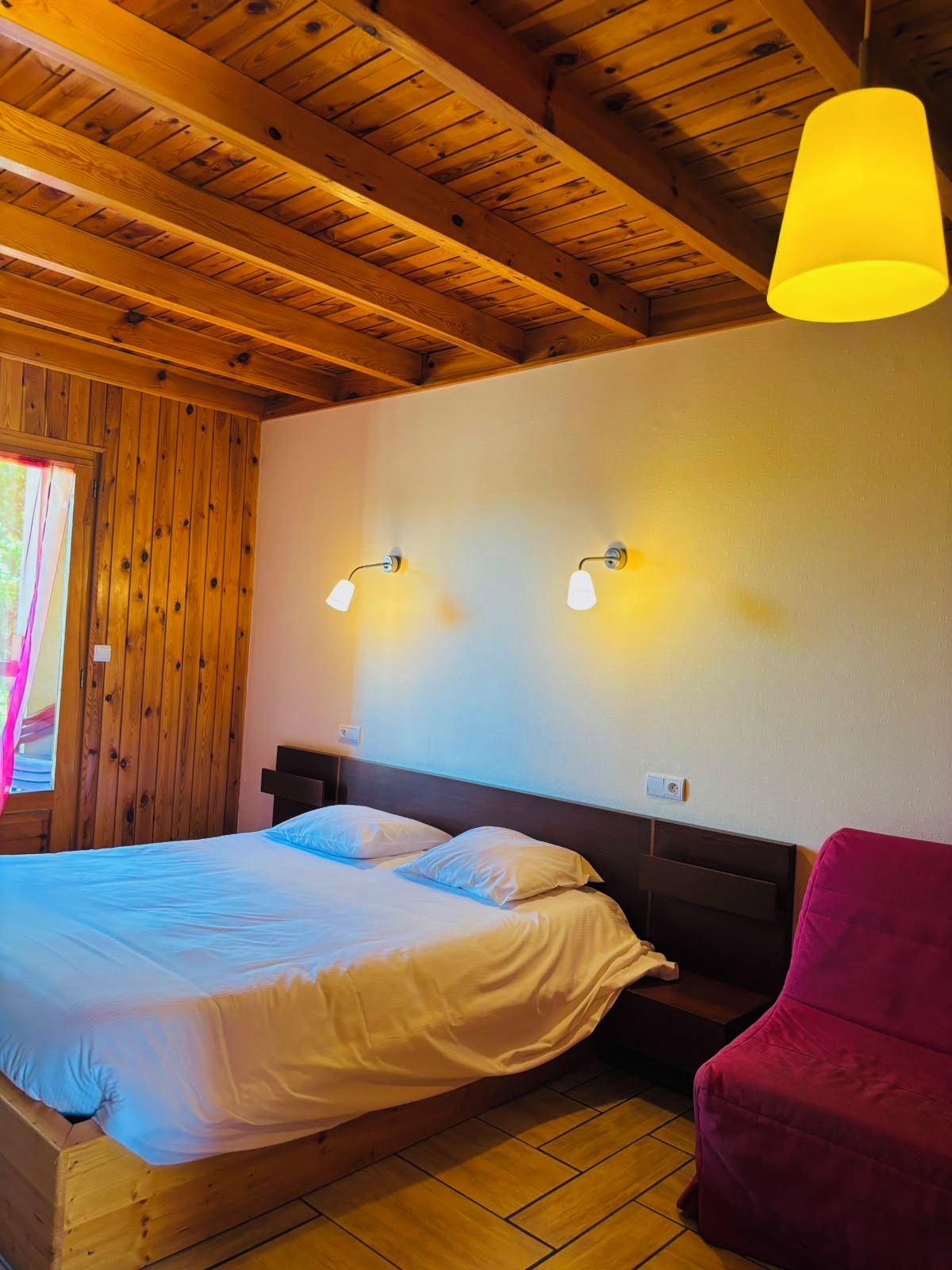 Habitación de cabaña de madera con una cama, dos luces fijadas a la pared y una lámpara colgante.