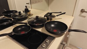 Eine Küche mit mehreren schwarzen Pfannen, einem Edelstahltopf und einem Herd mit Bedienelementen.