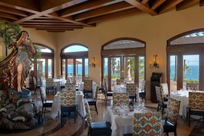 A restaurant with tables set for dining, large windows with ocean views, and a statue of a woman. - 1-bedroom junior suite in Pueblo Bonito Sunset Beach Resort Cabo San Lucas (Cabo San Lucas)