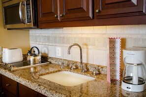 A kitchen with granite countertops, a stainless steel kettle, a toaster, a coffee maker, and wooden cabinets. - 1-bedroom junior suite in Pueblo Bonito Sunset Beach Resort Cabo San Lucas (Cabo San Lucas)