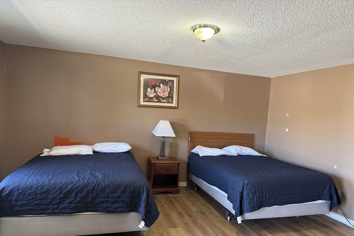 A hotel room with two beds, a nightstand, a lamp, and a painting on the wall.