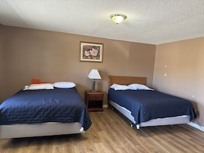 A hotel room with two beds, a nightstand, a lamp, and a painting on the wall. - Sparta Motel 7 (Sparta)