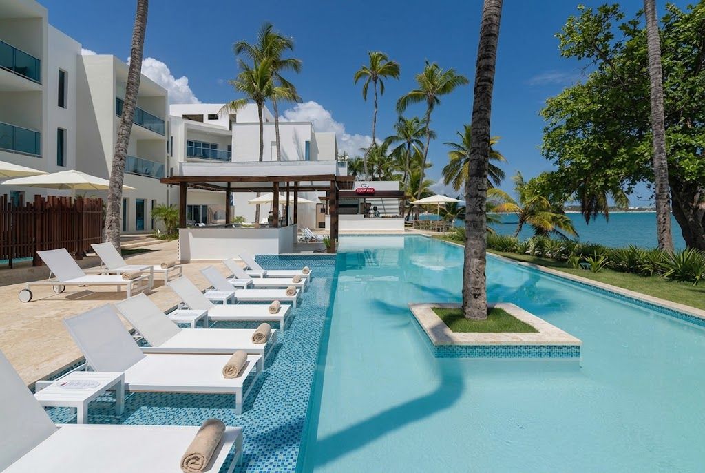 Ein Poolbereich mit Liegestühlen und einer überdachten Lounge, umgeben von Palmen und freiem Blick auf den Ozean.