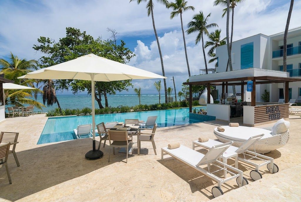 A poolside area with lounge chairs, a table, and umbrellas, overlooking a pool and the ocean.