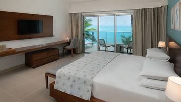 Habitación de hotel con cama, televisor montado en la pared, escritorio con silla y balcón con vista al océano.