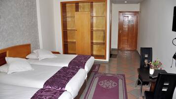 A hotel room with two beds, a wooden wardrobe, a desk with a chair, and a television.