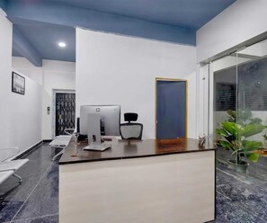 A reception desk with a computer, chair, and a door in a modern office space. - Classic Krishna Grand (Karīmnagar)