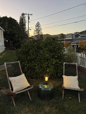 A backyard with two wicker chairs, a small round table with a lantern, and a dense green hedge. - Charming 2-bedroom house in centrally located Mill Valley neighborhood (Mill Valley)