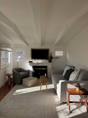 A living room with a fireplace, a sofa, a coffee table, and a television mounted on the wall. - Charming 2-bedroom house in centrally located Mill Valley neighborhood (Mill Valley)