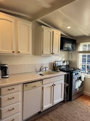 A kitchen with white cabinets, a dishwasher, a stove, and a coffee maker. - Charming 2-bedroom house in centrally located Mill Valley neighborhood (Mill Valley)