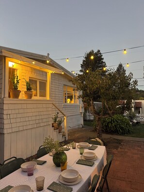 An outdoor dining area with a table set for two, potted plants, and string lights. - Charming 2-bedroom house in centrally located Mill Valley neighborhood (Mill Valley)