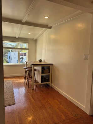 A room with a wooden floor, a small table with stools, a window with blinds, and a white wall. - Charming 2-bedroom house in centrally located Mill Valley neighborhood (Mill Valley)