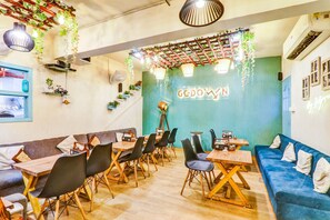 A cafe with wooden tables and black chairs, a blue sofa, and hanging plants. - Collection O Hotel Blueline (Kanpur)