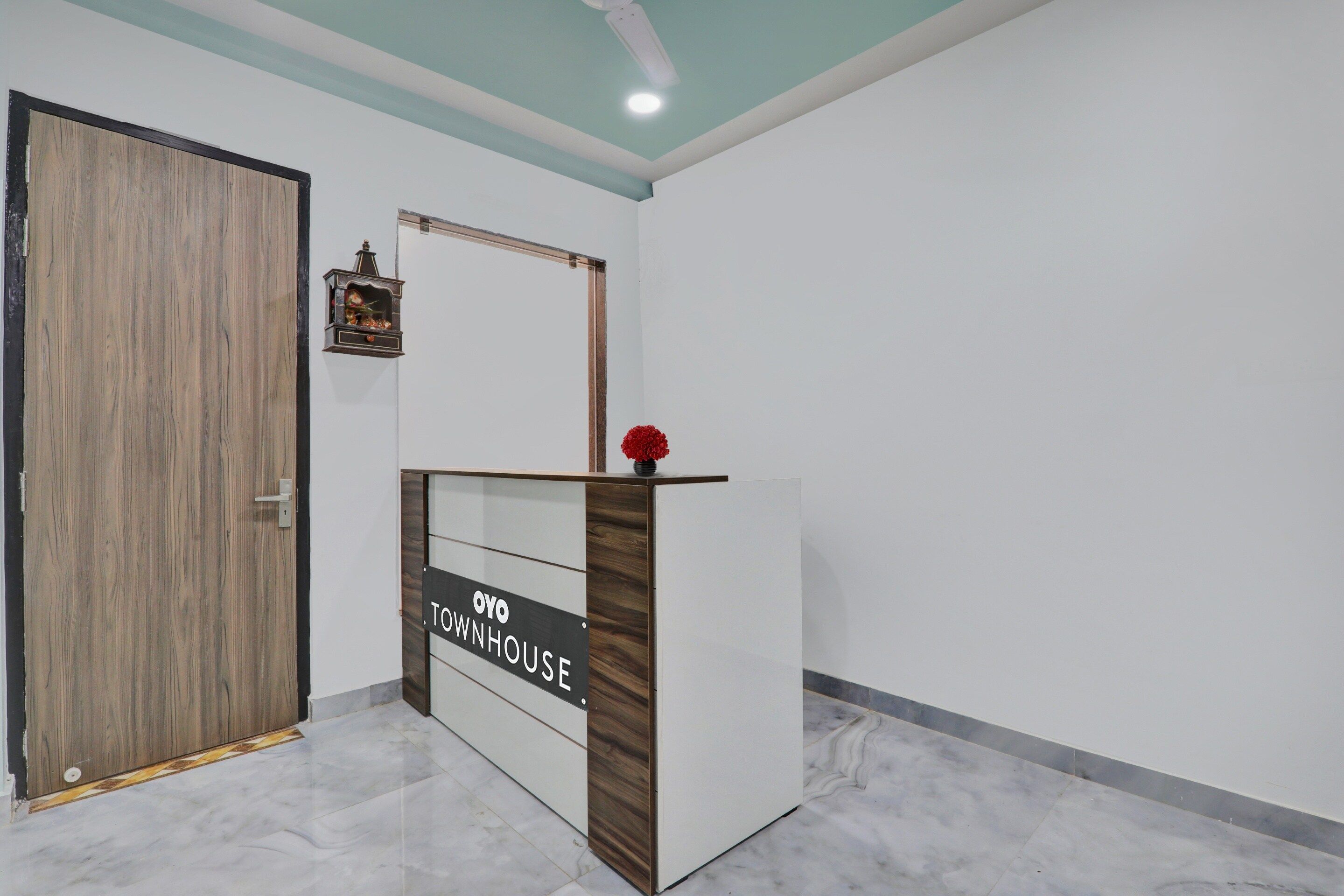 A reception desk with a sign reading 'OYO TOWNHOUSE' in a modern interior with a wooden door and a ceiling light.
