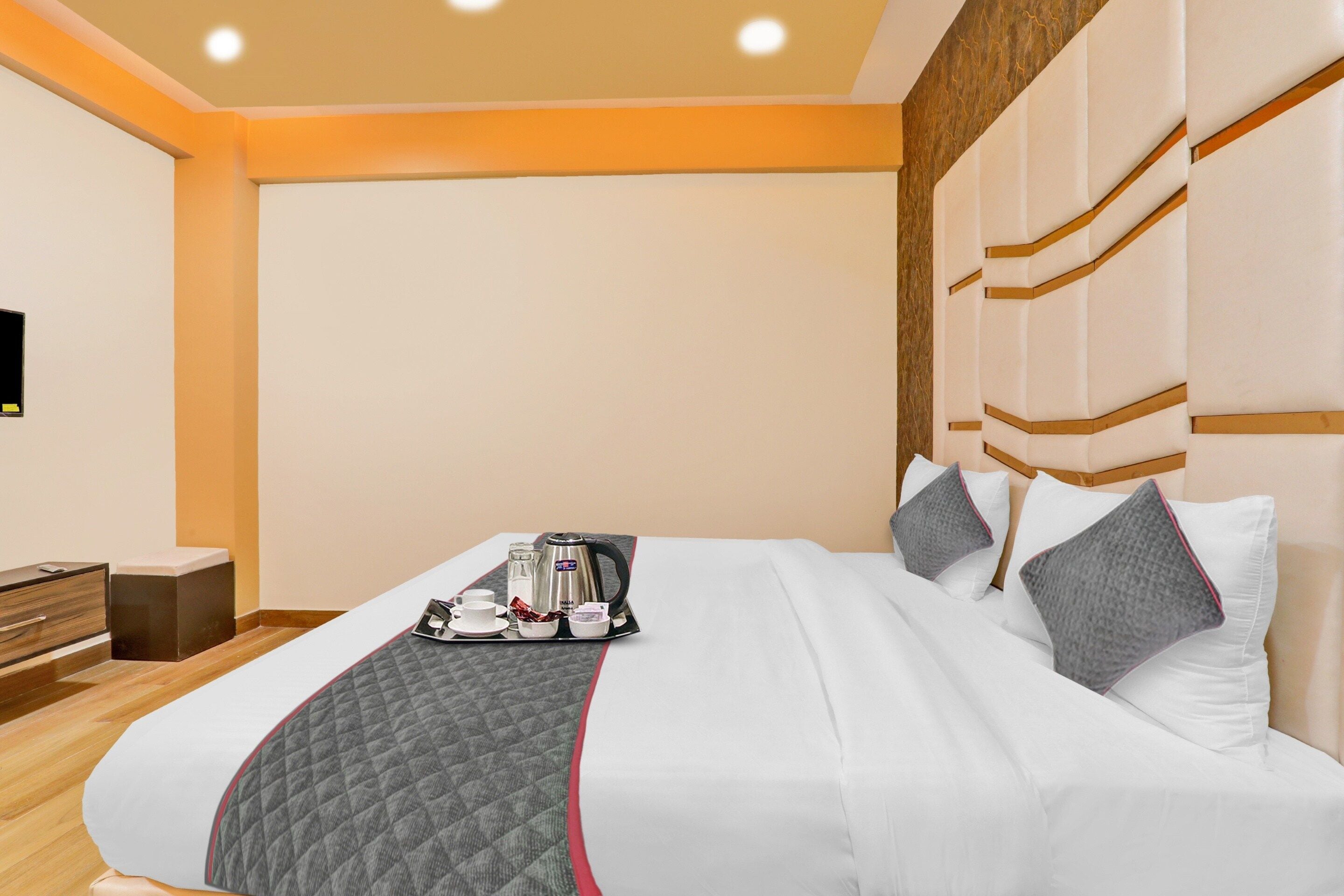 A hotel room with a bed, a bedside table, a TV, and a tray with a kettle and cups.