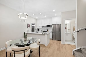 A modern kitchen with white cabinetry, stainless steel appliances, and a glass dining table with chairs.