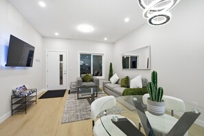 A modern living room with a flat-screen TV, a glass dining table, and a cactus plant. - Spacious Home 5 mins from Downtown & Close to everything (Calgary)