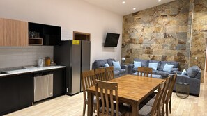 A modern kitchen with a dining area, stone wall, and grey sofas. - VILLA ALESSANDRA – TU ESCAPADA PERFECTA EN BAJO BOQUETE (bajo Boquete)