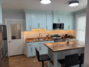 A kitchen with light blue cabinets, a microwave, a stove, and a sink. There are two chairs and a small island with a glass top. - Charming 3-bedroom apartment in lovely Utica (Utica)